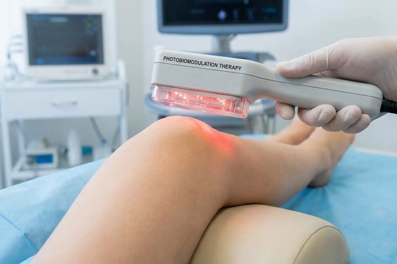 Performing cold laser therapy on a patient’s knee.
