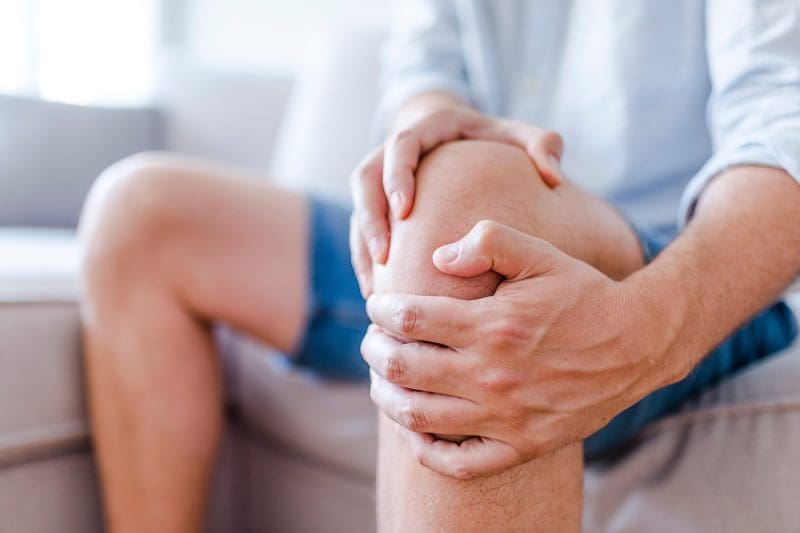 A man sitting in a sofa with knee pain.